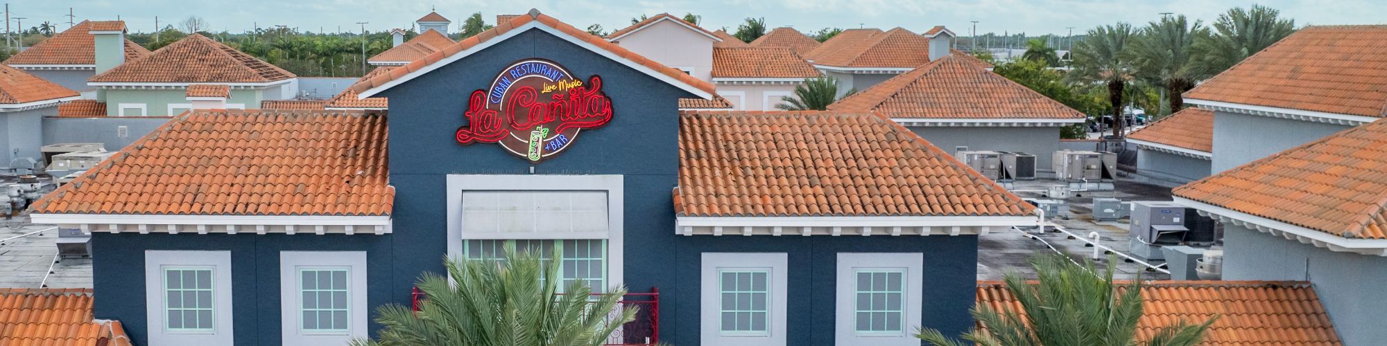 A colorful strip of storefronts with orange-tiled roofs, palm trees, and a blue building featuring a red dragon crest in the center.