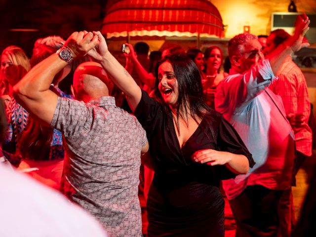 People dancing in a lively club with red lighting, a smiling woman in black center, others swaying and enjoying the party atmosphere.