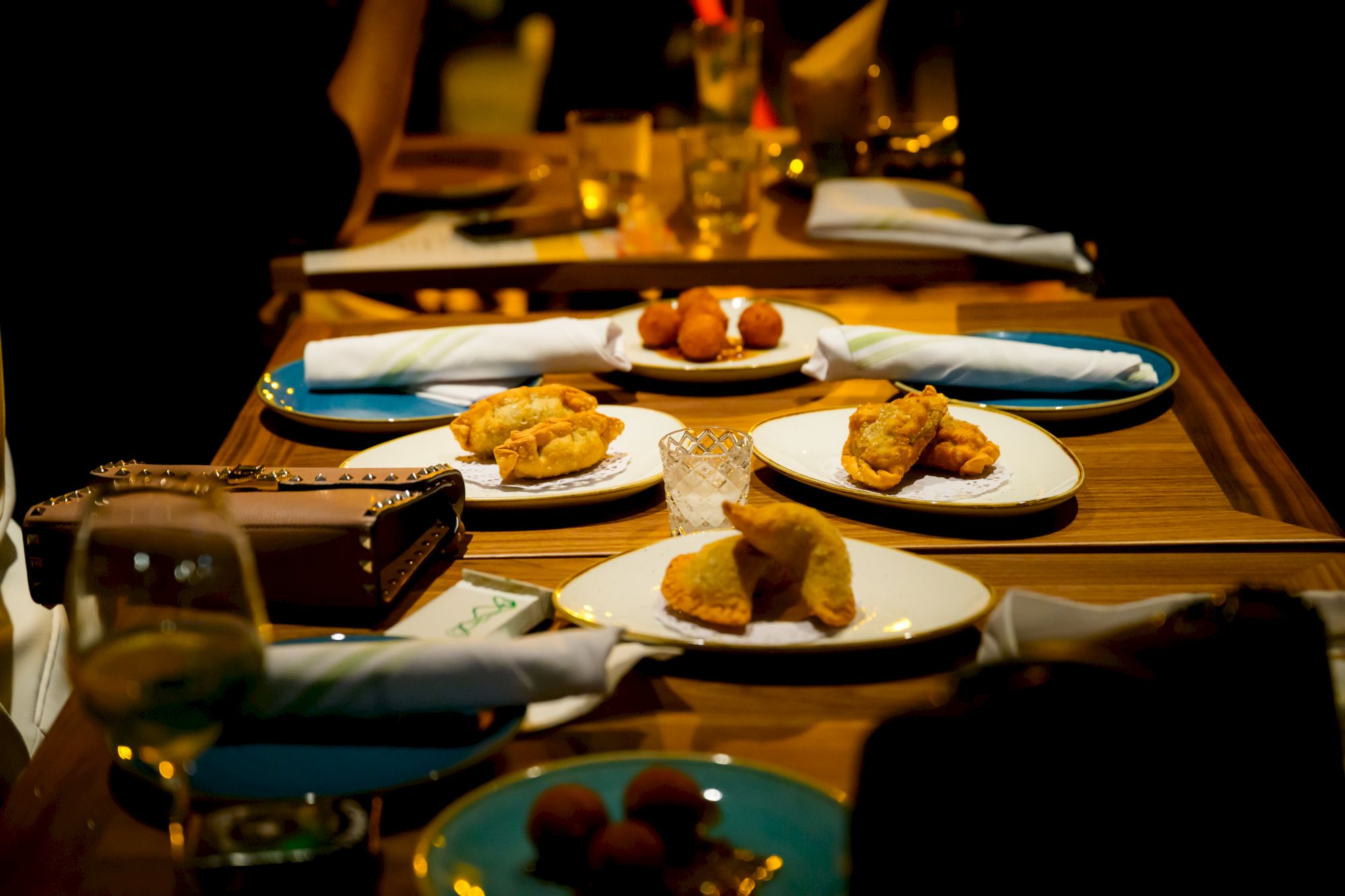 A romantic table setting with multiple small plates of fried foods and desserts, wine glasses, and a candlelit dinner vibe.